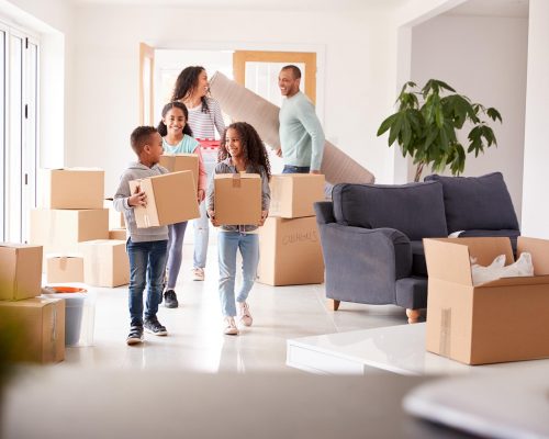 Smiling Family Carrying Boxes Into New Home On Moving Day